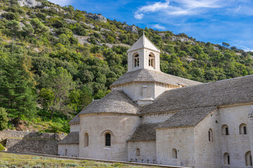 View of Senanque Abbey's stone structure rising above rows of lavender fields under a clear sky, a serene blend of nature and architecture, Gordes, Provence-Alpes-C&ocirc;te d'Azur, France.