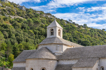 View of Senanque Abbey's stone structure rising above rows of lavender fields under a clear sky, a serene blend of nature and architecture, Gordes, Provence-Alpes-C&ocirc;te d'Azur, France.