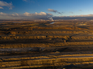 High resolution panoramic view of an open pit coal mine with mining machines, layered terrain. Industrial landscape showing large scale extraction, energy production, and environmental impact.