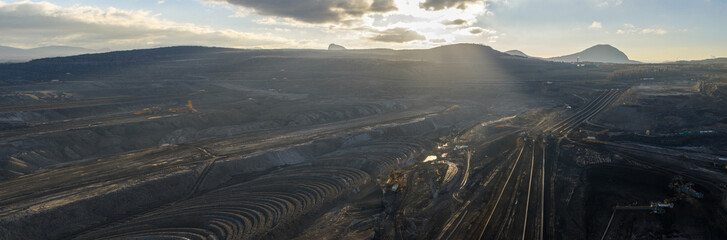 High resolution panoramic view of an open pit coal mine with mining machines, layered terrain. Industrial landscape showing large scale extraction, energy production, and environmental impact.