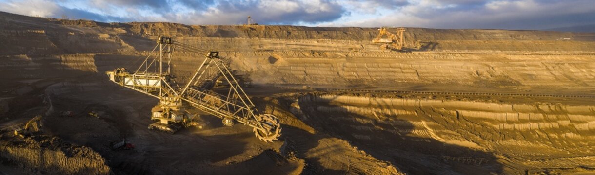 High resolution panoramic view of an open pit coal mine with mining machines, layered terrain. Industrial landscape showing large scale extraction, energy production, and environmental impact.