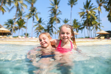 Happy children in a swimming pool on an exotic holiday, laughing and enjoying a carefree vacation in a tropical resort.