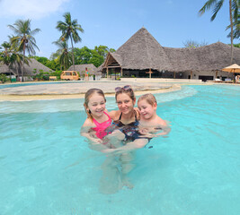 Two cheerful children with their mother while enjoying a luxury tropical vacation at a resort swimming pool.
