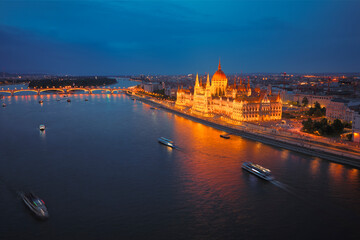 Panoramic evening view of Budapest during the blue hour, featuring the illuminated Hungarian Parliament and Margit Bridge reflected in the Danube river