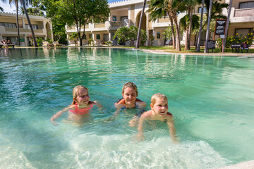 Two cheerful children with their mother while enjoying a luxury tropical vacation at a resort swimming pool.