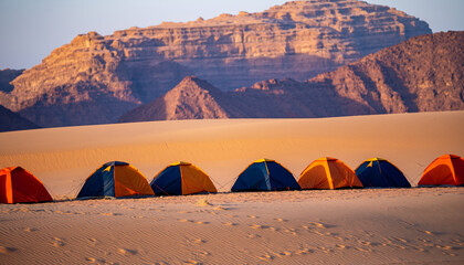 Colorful expedition tents lined up on pristine sand dunes with dramatic red rock formations. Perfect for adventure travel, outdoor recreation, and wilderness camping content