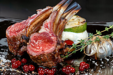 Rack of Lamb - The meat is cooked to medium rare, giving it a pink hue and a tender texture. The dish is garnished with roasted garlic, red currants, and a sprig of rosemary