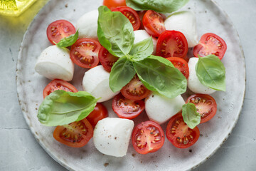 Caprese with bocconcini, red cherry tomatoes and green basil on a grey plate, horizontal shot,...