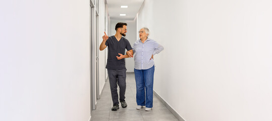 Elderly woman listening as male doctor pointing away and explaining health information in hospital corridor