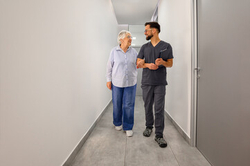 Male ophthalmologist walking arm in arm with senior woman during eye-care discussion in hospital lobby