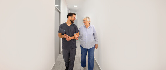 Senior woman and male doctor walking arm in arm while discussing medical guidance and treatment options in hospital lobby