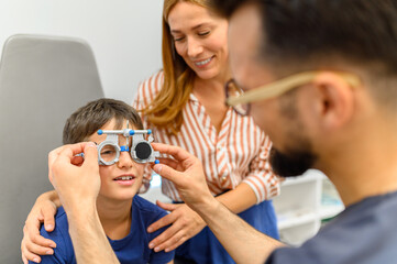 Smiling mother observing son while male doctor adjusting phoropter lenses during eye test during vision assessment at clinic