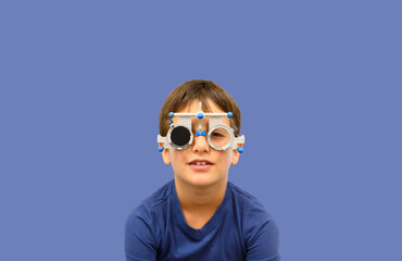 Portrait of boy wearing phoropter lenses looking at camera against blue background during ophthalmology exam