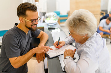 High angle view of male receptionist guiding senior patient while filling medical document at hospital desk