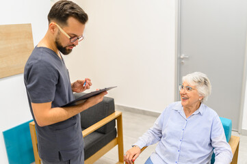 Confident male doctor discussing medical records with senior woman seated in the waiting room during visit