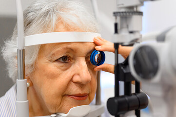 Close-up of ophthalmologist hand holding slit lamp lens for senior woman eye examination at clinic