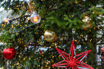 Close up detail of christmas tree decorations with red and gold baubles, star shaped ornaments and warm lights imitating fire, festive holiday atmosphere in brno city