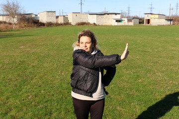 Fototapeta premium Woman performing arm and torso stretching exercise outdoors on green field