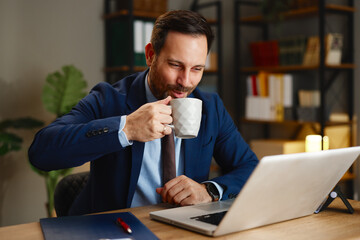 Businessman drinking coffee while working on laptop in modern office