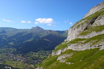 Fototapeta premium Panoramic view of Grindelwald valley with alpine village, green meadows, and Swiss mountain peaks