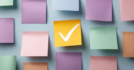 Colorful sticky notes arranged on a surface with one yellow note featuring a white check mark symbolizing completion or approval