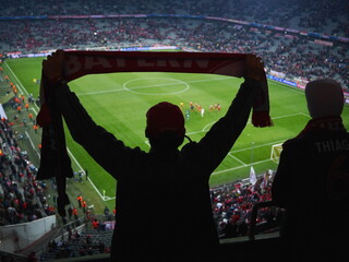 Man is holding a red scarf and is watching a soccer game