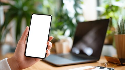 Modern workspace with smartphone in hand, laptop and plants conveying productivity and technology in a bright environment