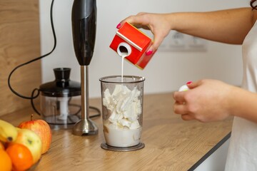 Woman pouring milk into blender for smoothie