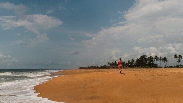 Woman walking alone on a golden sandy beach in Cotonou, Benin
