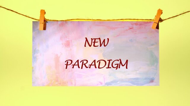 New Paradigm appears on a delicate, watercolor-painted canvas, hung gracefully with tiny, wooden clothespins against a cheerful yellow backdrop