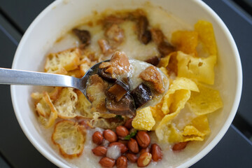 Chicken and mushroom rice porridge with creamy smooth texture, savory toppings, crunchy crackers, peanuts, herbs, and warm comforting flavor, modern Asian breakfast dish with clean appetizing presenta