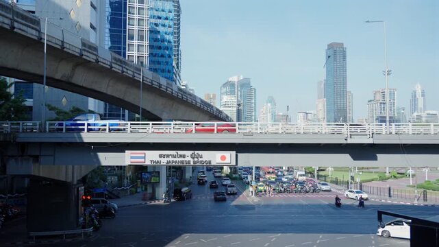 Traffic Flow Under Thai-Japanese Bridge in Silom, Bangkok, Urban City Intersection with Cars and Motorbikes, Modern Cityscape and Transportation, Daytime