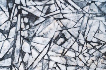 Close-up abstract texture of fractured white ice pieces creating a geometric mosaic pattern on a dark background, representing winter, cold, or a broken surface.