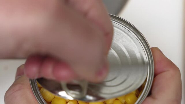 A can of sweet corn is opened by hand in a close-up kitchen shot. The video highlights food preparation and everyday cooking ingredients