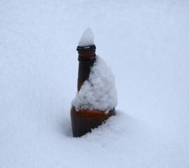 A dark glass beer bottle lies in a snowdrift