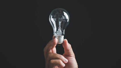 Hand holding a lightbulb against a black background. Concept of ideas, innovation, and solutions. .