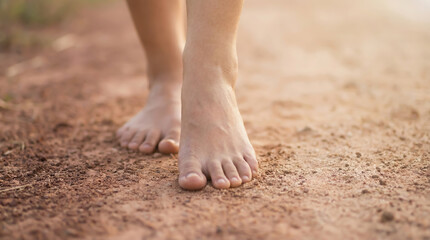 Close-up of bare feet walking on a dry reddish dirt road on a sunny day