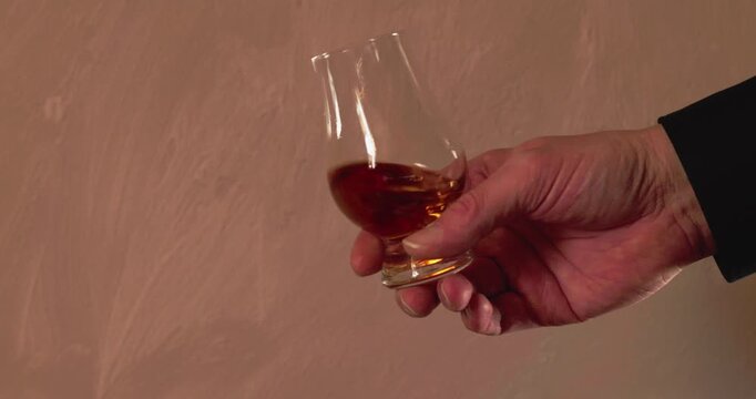 Eine m&auml;nnliche Hand schwenkt ein Glas w&auml;hrend einer Whiskeyverkostung, Zeitlupe.