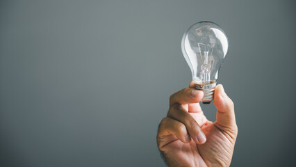 Hand holding a lightbulb against a gray background, symbolizing a new idea or solution.