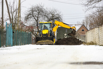 Two machines work on a snowy road, moving dirt and debris in a rural area on a winter day