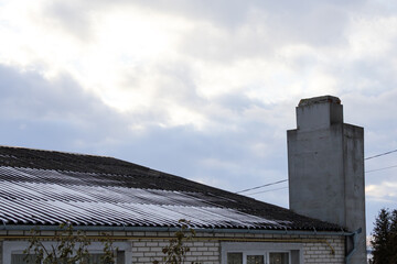 A house has a sloped roof with some snow on it and a tall chimney. The sky is cloudy with shades of gray