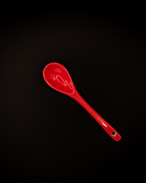 Minimalist studio photograph of a glossy red ceramic spoon isolated on a black background. The image features strong contrast, smooth reflective surface, and clean composition.