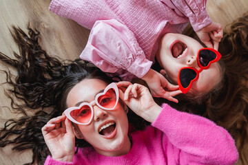 Cute little girl with her teenage sister in heart glasses on a background of pink balloons....