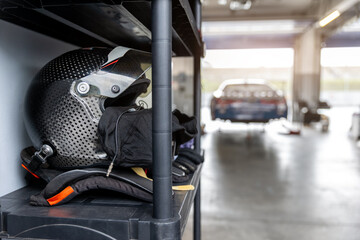 Carbon racing helmet resting shelf inside motorsport garage with blurred race car background conveying preparation speed. Professional pitlane atmosphere highlights performance engineering