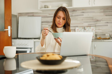 Business woman using laptop computer while having breakfast at home
