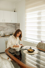Business woman working remotely from home taking notes while having online meeting