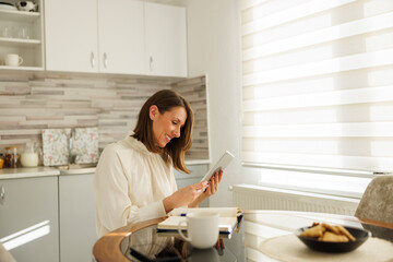 Woman writing notes in planner and using tablet computer while working remotely from home