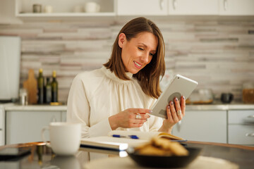 Woman writing notes in planner and using tablet computer while working remotely from home