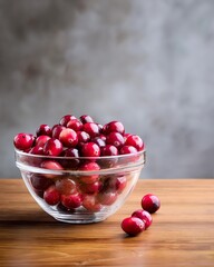 A glass bowl filled with vibrant red cranberries, set on a wooden surface, showcasing freshness and natural beauty.