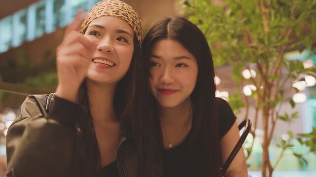 Two young asian woman gen z sisters scrolling on phone browsing at shopping mall and dating app online
